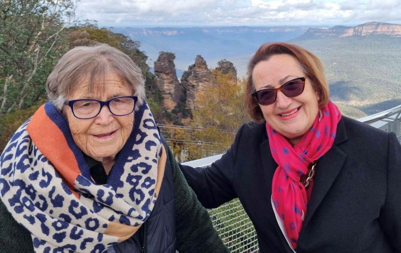 Gordana stands with one hand on her mother Ljubica's back in front of the Three Sisters rock formation in the Blue Mountains