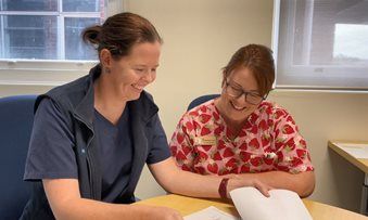 Image of Bianca Jones mentoring Charmaine Savanah, a student midwife. Both are seated at a table and looking at paperwork together.