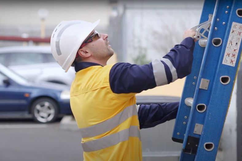 A worker wearing personal protective equipment, using an extension ladder.