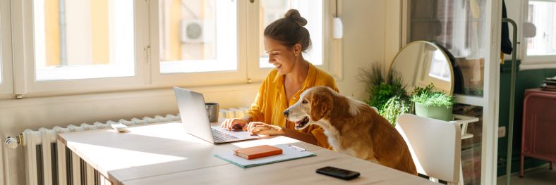 A young woman working from her home office with her pet dog.
