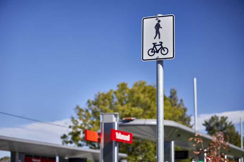 A shot of a shared path sign standing before a light-rail station and a bright cloudless day