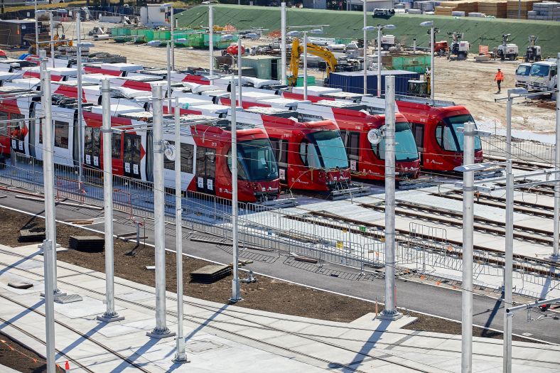 A distant shot of several stationary light rail vehicles in the stabling yard on a bright day.