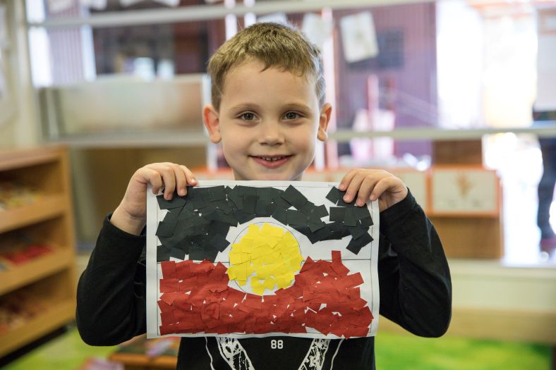A young boy holds an artwork of the Aboriginal flag