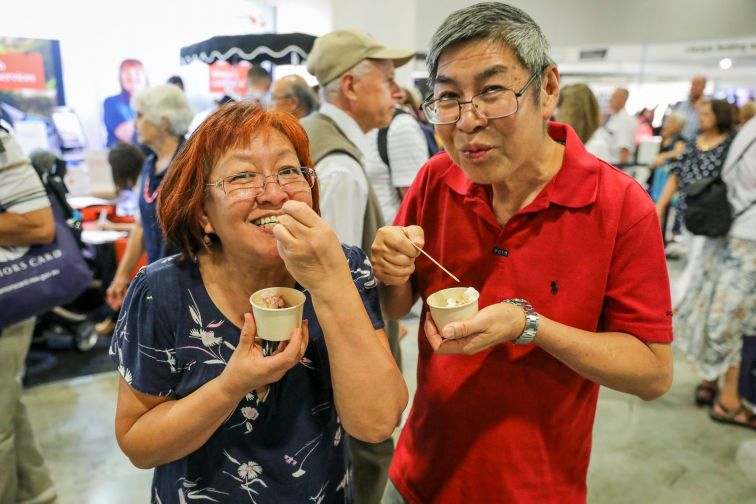 Woman and man smiling with delight at tasty icecream they're scooping from cups at Seniors Expo