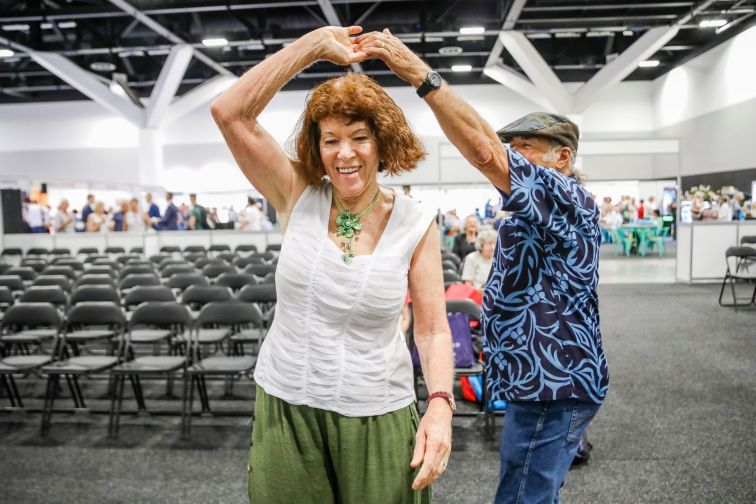 Woman spins around under her partner's arm, dancing in casual clothes at Seniors Festival event