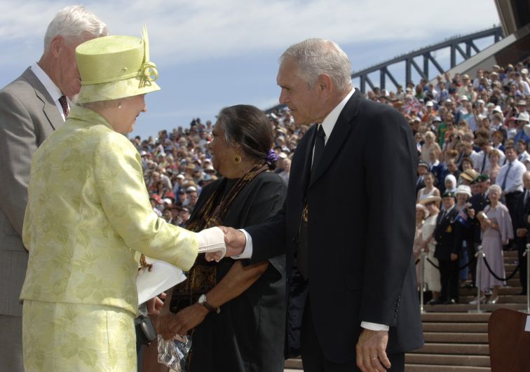 Her Majesty Queen Elizabeth II is meeting with two other dignitaries on the steps of the Sydney Opera House  Her Majesty is wearing a light lime green skirt and jacket with a matching hat. 