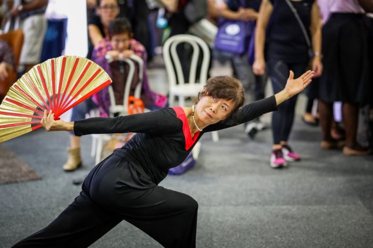woman balances and poses with an outspread fan at Seniors Expo