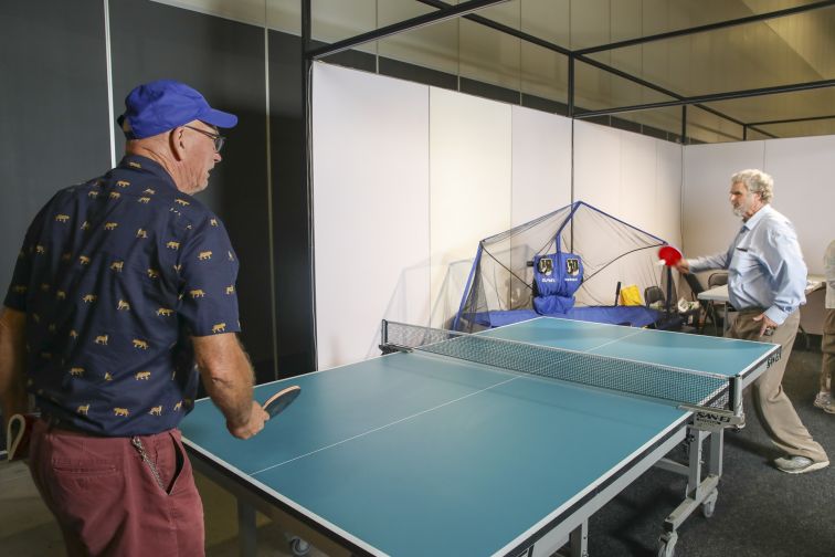 Photo of two senior men playing table tennis on a teal coloured table tennis table. 