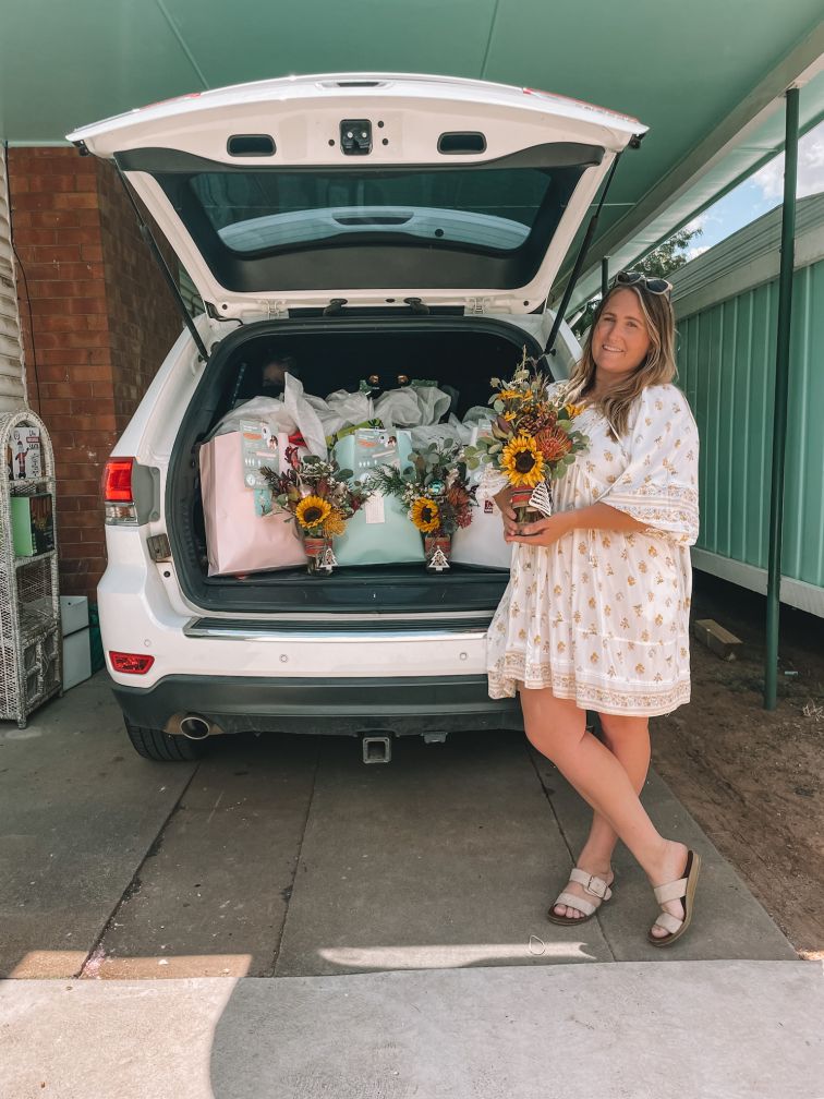 Women in white dress holding flowers next to car with boot open