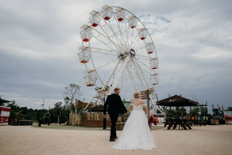 A candid photo of a couple walking in front of a ferris wheel