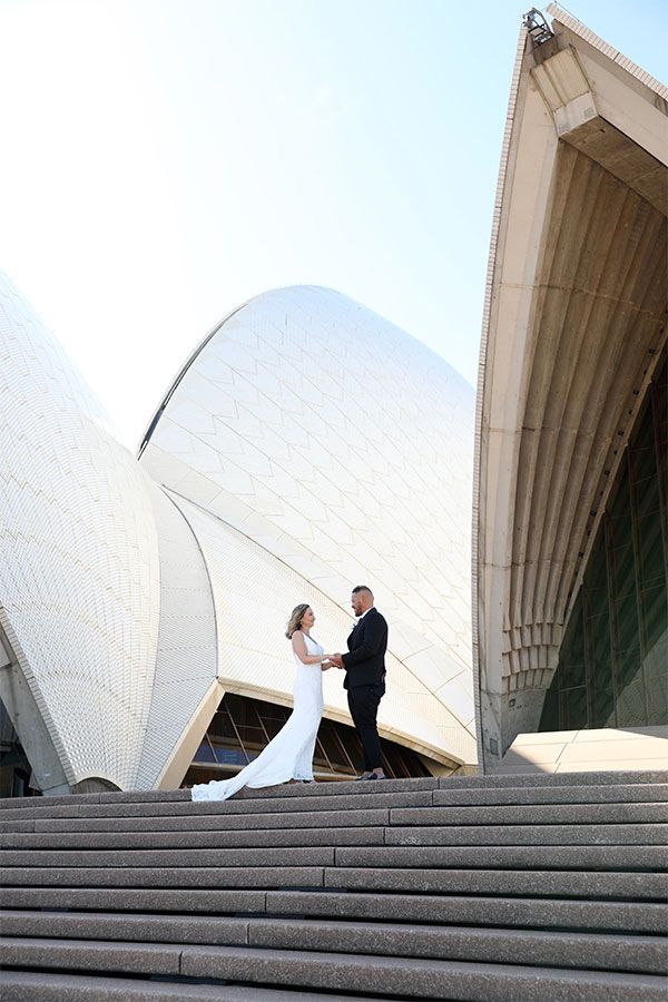 A couple hold hands outside the Sydney Opera House