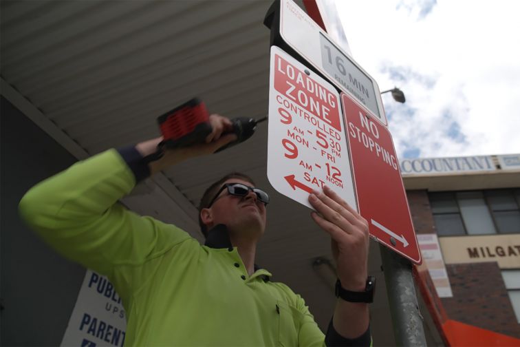 A person installs a digital parking sign in Campbelltown for the Smart Digital Kerbside project.