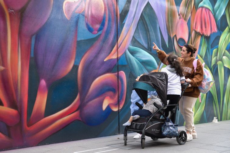 A woman pushes a pram with a child inside, while looking at a painting on an outdoor wall in Liverpool.
