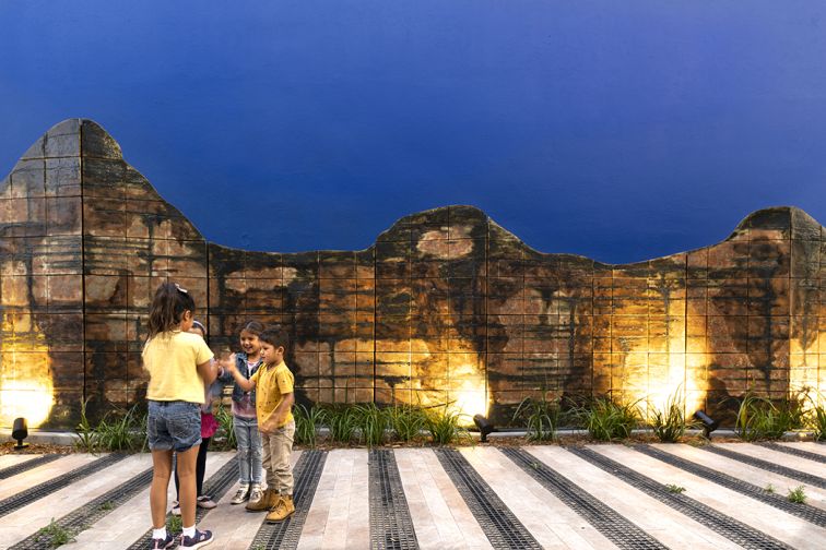 Children play beside artistic stone-look wall embellished by lights below