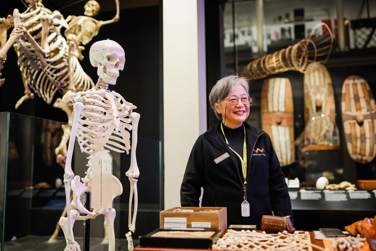 smiling volunteer next to an exhibit with a skeleton