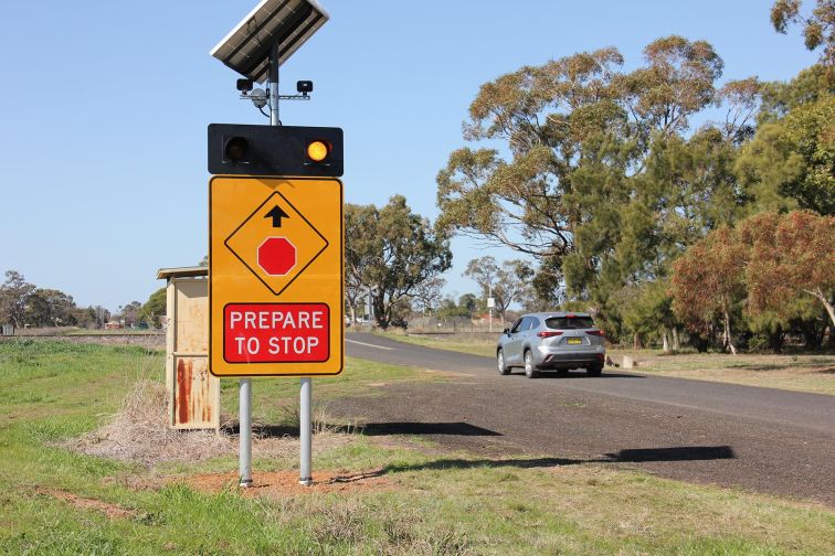 A car drives past a smart sign in Narromine, with flashing lights warning the driver to prepare to stop at the level crossing ahead.