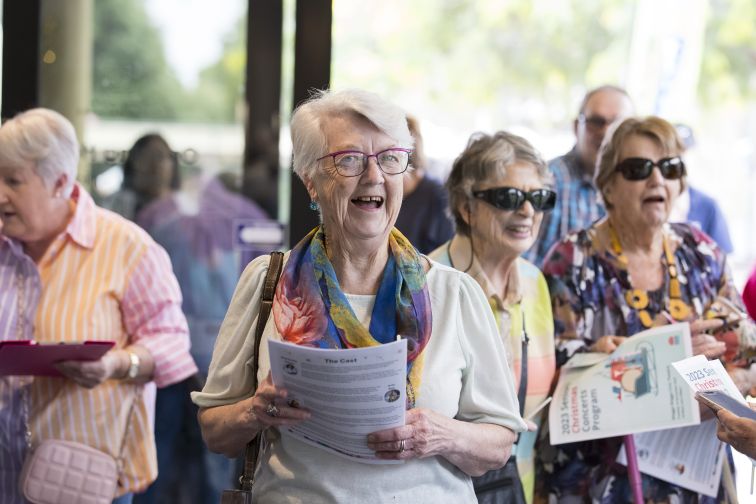 Older woman smiling to camera holding program.