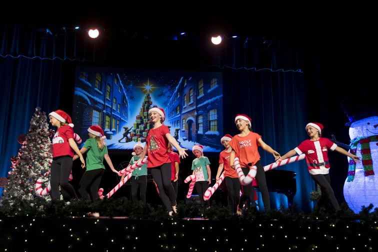 School kids performing Christmas dance on stage, holding candy canes.