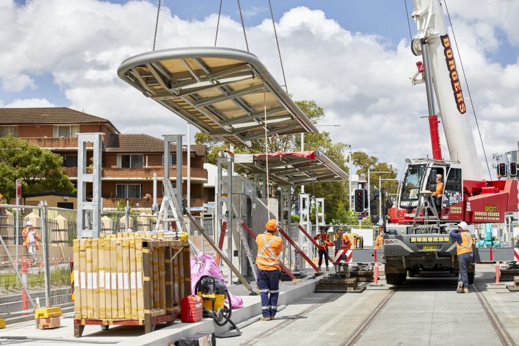 Construction workers alongside a crane installing a canopy at a new light rail stop.