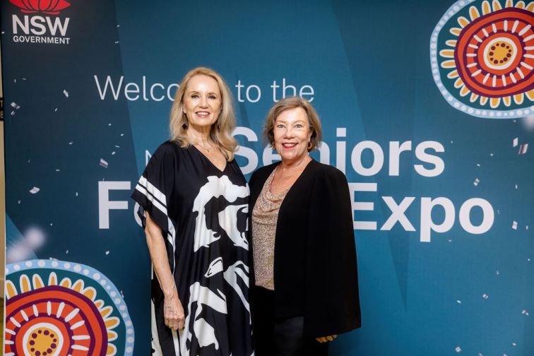 two female seniors standing in front of Expo media wall