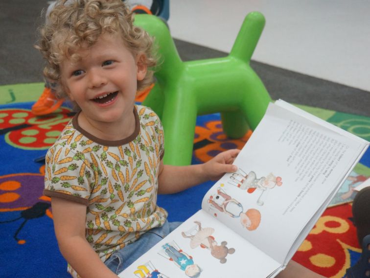 A toddler boy smiles while reading a picture book.