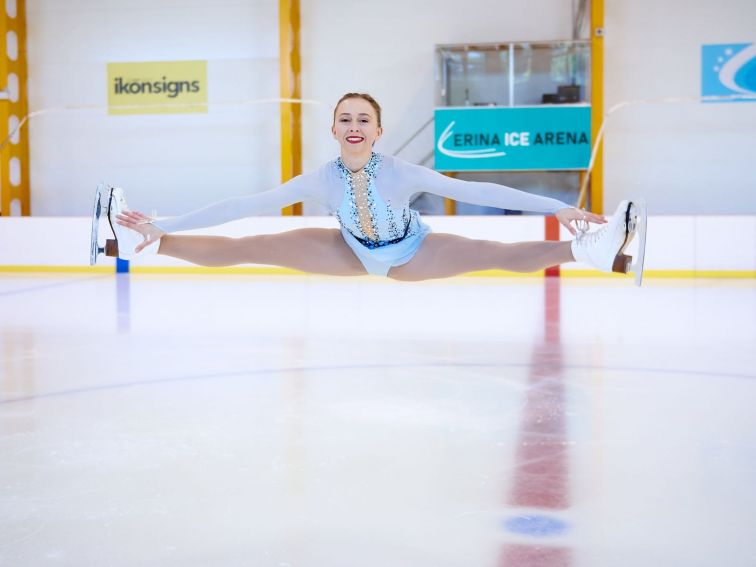 Figure Skater has jumped in the air into a split position reaching for her toes.