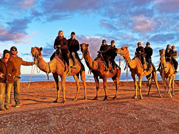 A group of eight people smiling as they enjoy a Silverton Sunset tour with Silverton Outback Camels.