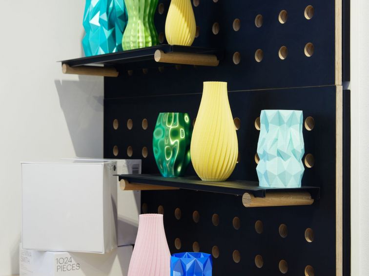 Rows of colourful, 3D printed vases on black shelves