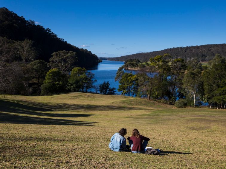 2 people sitting on grass overlooking a river