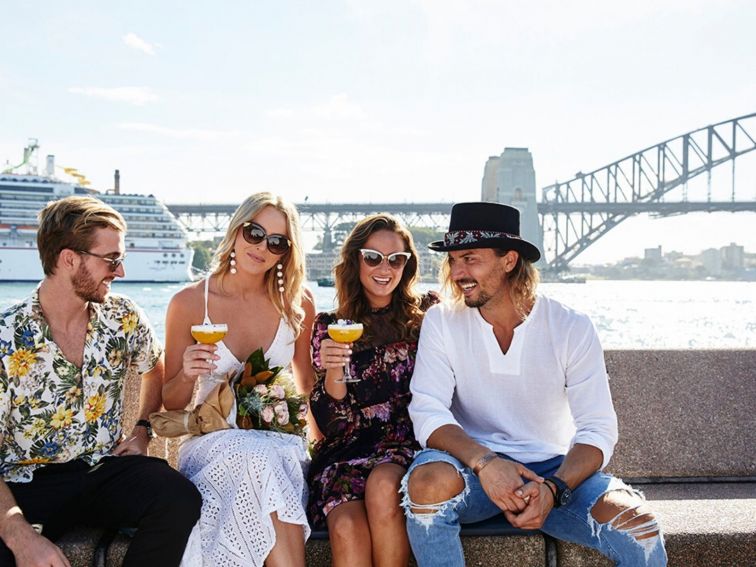 Four friends enjoying drinks in the sunshine with Sydney Harbour Bridge in the background