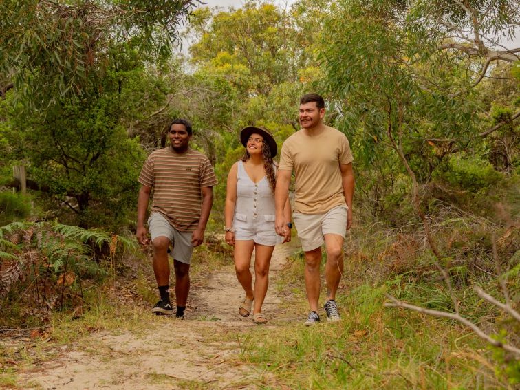 Two men and a lady walking through the bush on a path.