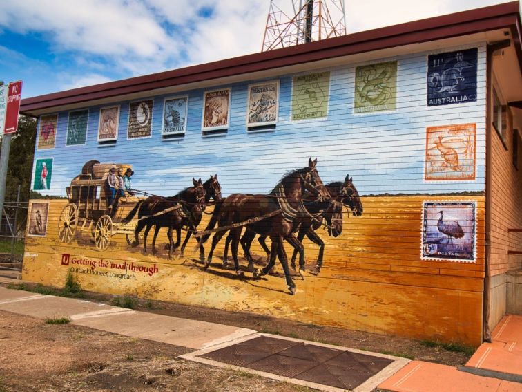 A mural on a brick wall featuring a horse and carriage with postal stamps around the border.