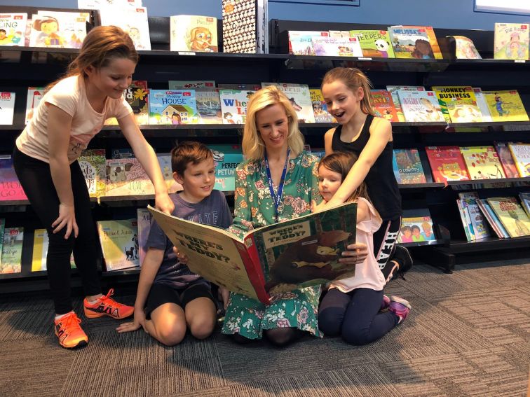 A librarian reads a picture book to 4 interested kids