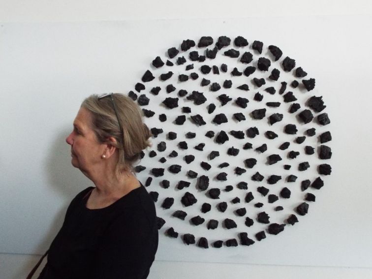 Woman standing in front of wall sculpture made os charcoal lumps
