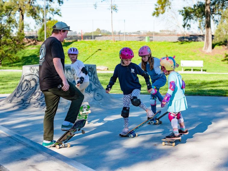 A group of young girls learning flat ground basics on their skateboard.