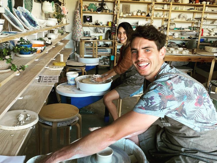 picture shows a male and female smiling sitting on a pottery wheel