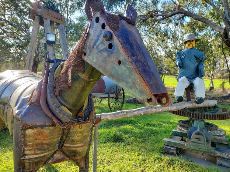 A closeup of a metal horse sculpture with a sculpture of a man at a pump in the background.