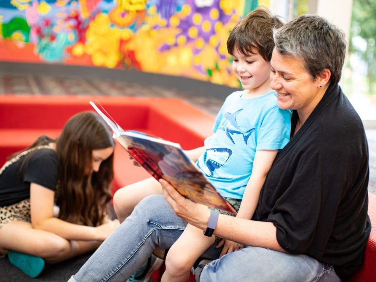 A parent reads a picture book to a young child in the colourful children's area.