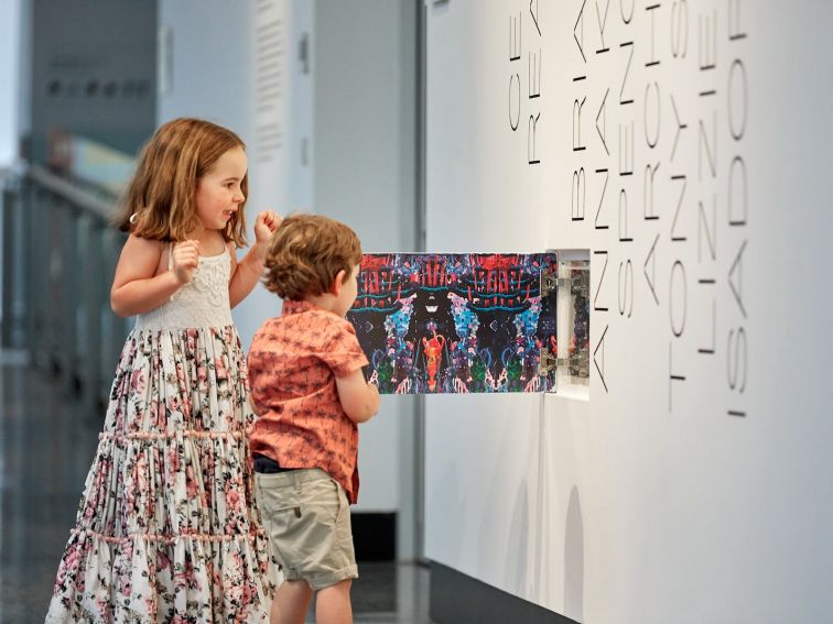 Two children open a cupboard with an art installation inside
