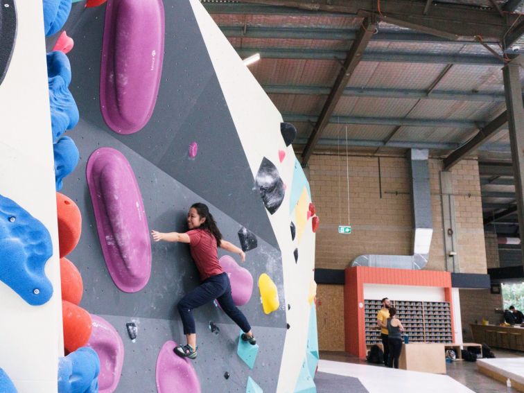 a climber is smiling, on the wall amongst large purple holds