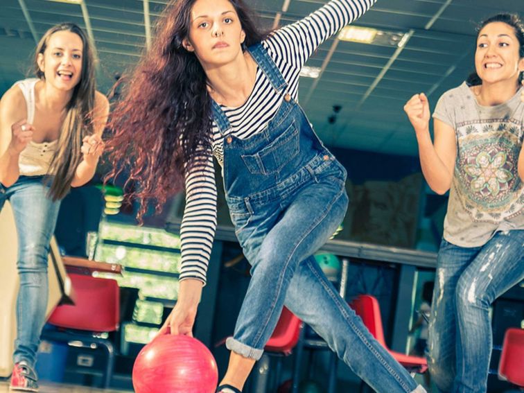 Young women bowling surrounded by friends cheering