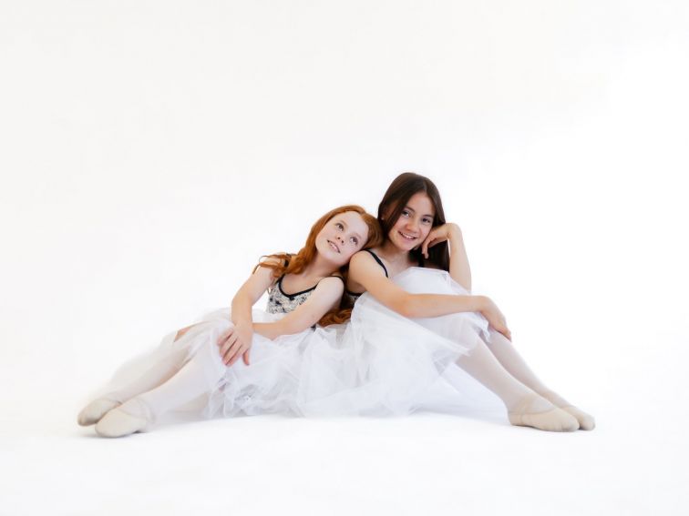 Two ballet students sitting together in white skirts and floral leotards
