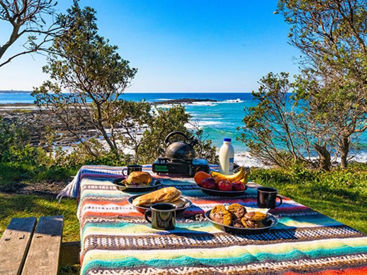 A picnic table filled with a feast, overlooking the beach at Angourie Bay picnic area in Yuraygir