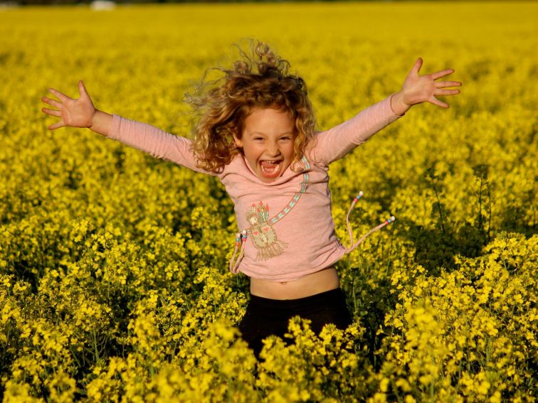 Excited girl in canola field with arms wide open