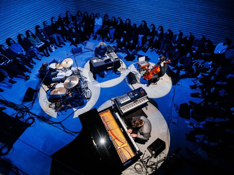Birds eye view of a four piece jazz band perform with a crowd seated around them