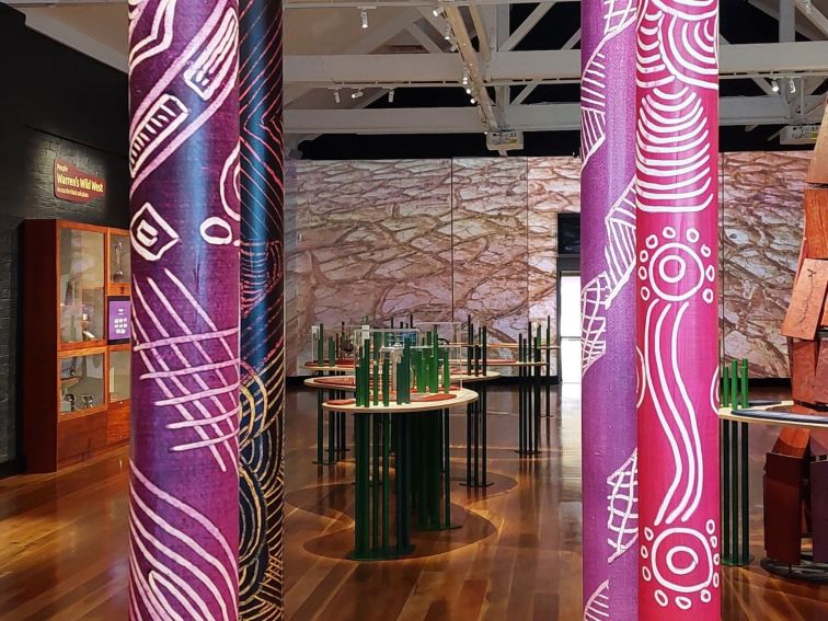 Photo of interior of Museum with painted poles evoking mes with audio/vvisula display in sage sticks