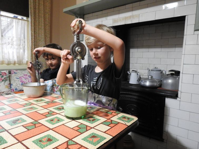 Two young children using hand food beaters in museum kitchen