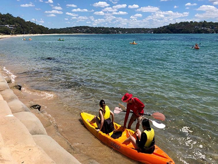 People being helped into a kayak in ocean, at Bonnie Vale picnic area. Photo: OEH/Natasha Webb