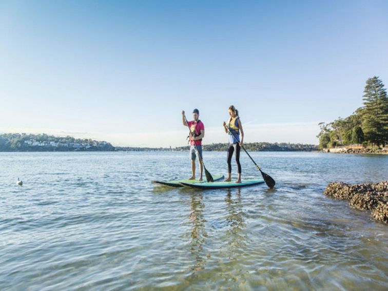 Two people stand-up paddle boarding in Cabbage Tree Basin, next to Bonnie Vale picnic area in Royal