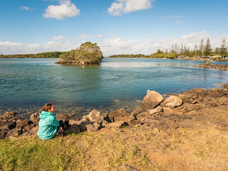 A woman sitting by the water at Brunswick River picnic area in Brunswick Heads Nature Reserve.